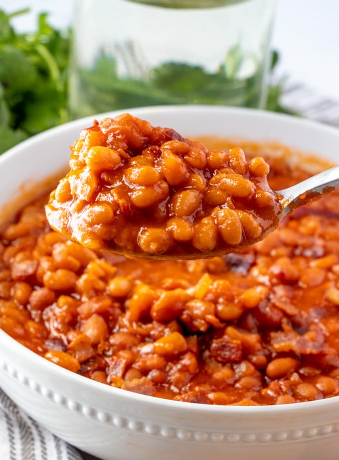 a bowl of baked beans, a spoon lifting up a serving.