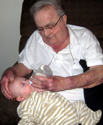 A grandpa sitting in a recliner and holding his infant grandson