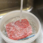 A bowl of water with plastic wrapped ground beef