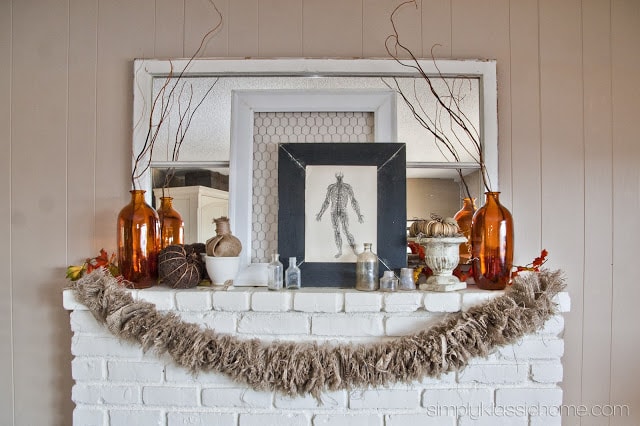 White mantel with fall decor including pumpkins, burlap, vintage anatomy print, and amber colored vases