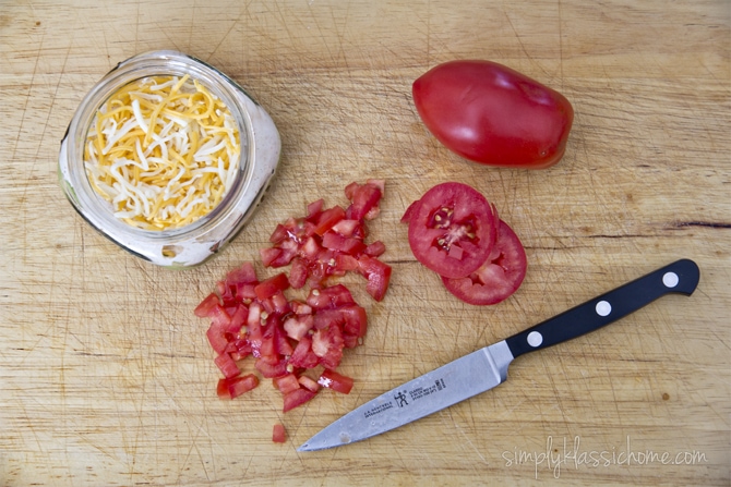 A knife sitting on top of a wooden cutting board, with tomatoes and cheese