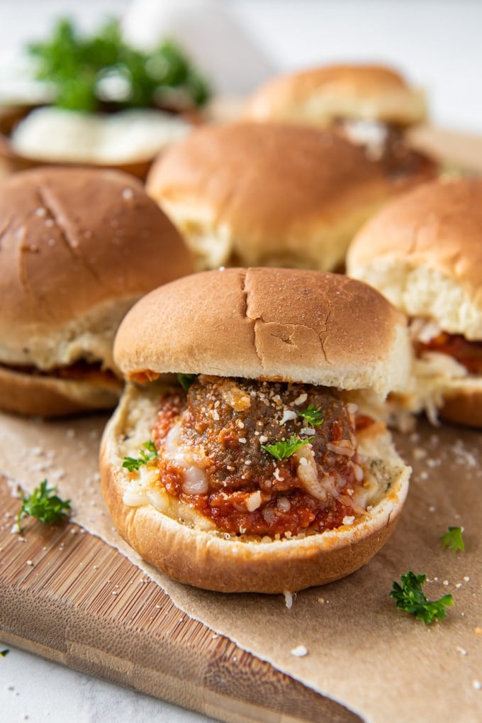 a slider roll with a meatball, sauce and cheese with several more in the background.