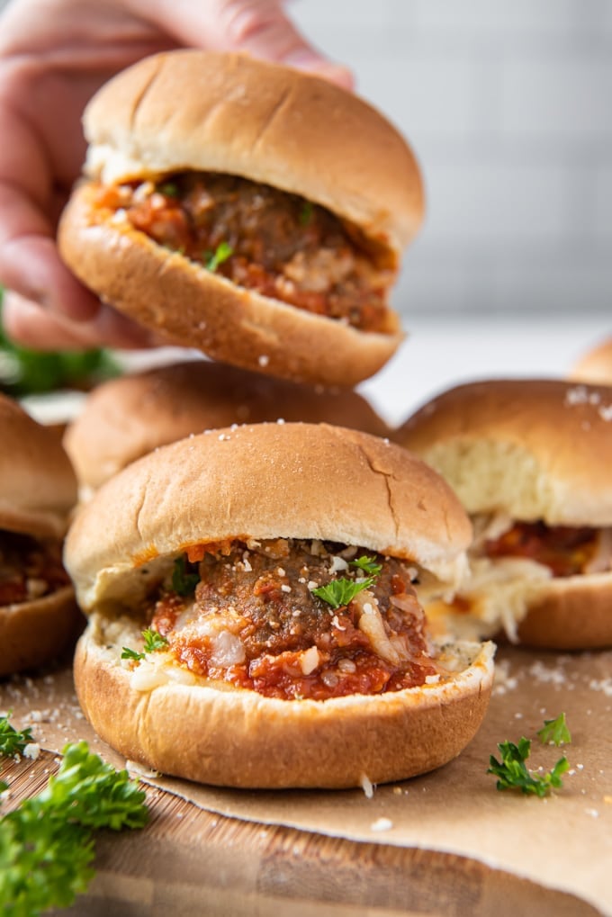 a hand reaching in and taking one of several meatball sliders