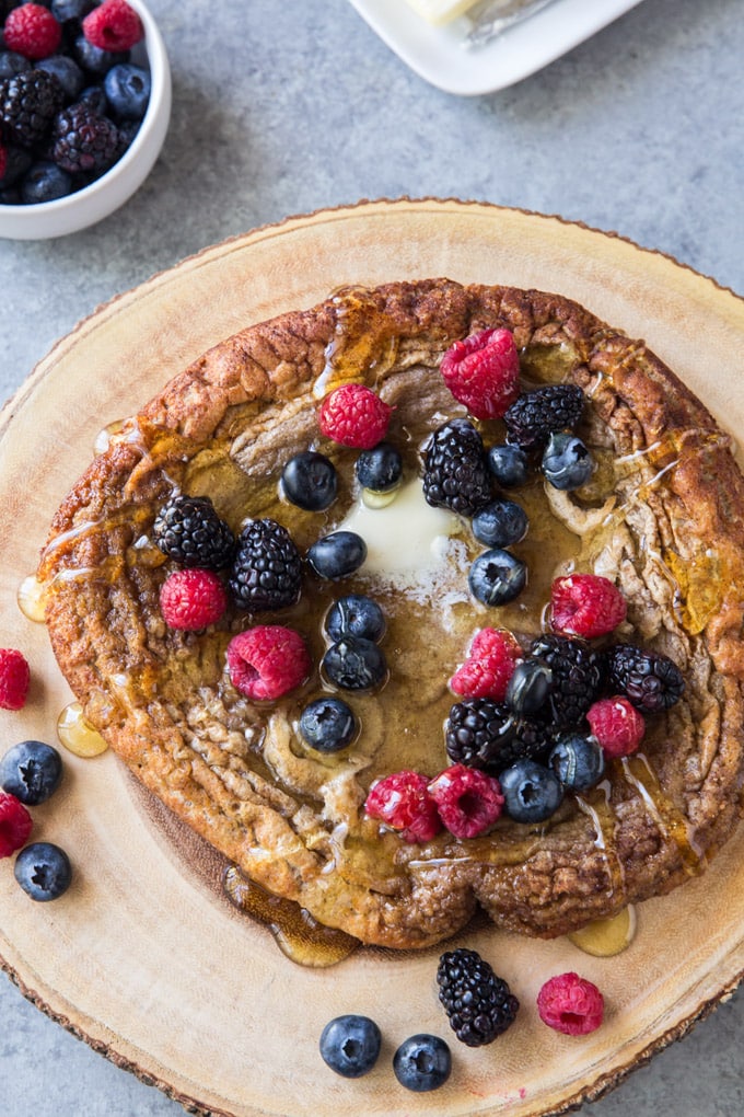Oven Baked Pancake, round, on a wood slice with berries on top. 