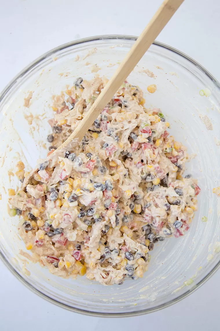 Skinny Southwest Chicken Dip is full of shredded chicken and loads of veggies and spices for a healthy Southwest Chicken Salad appetizer or main course! Skinny Southwest Chicken Salad mixed together in a bowl with a wooden spoon