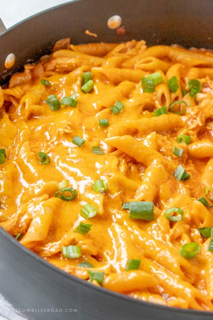 One pot cheesy chicken pasta in a pan with melted cheese and sliced green onions on top.