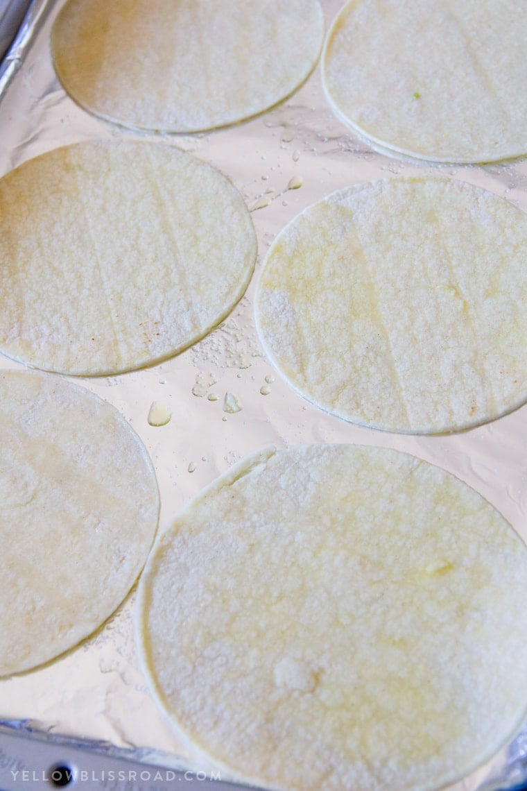 Corn tortillas on a baking sheet brushed with oil.