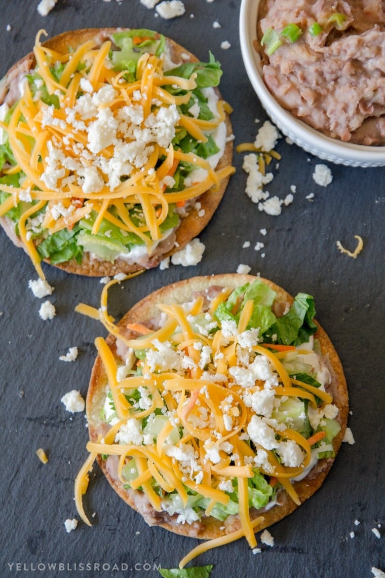 An overhead shot of two tostada shells topping with refried beans, lettuce and cheese.