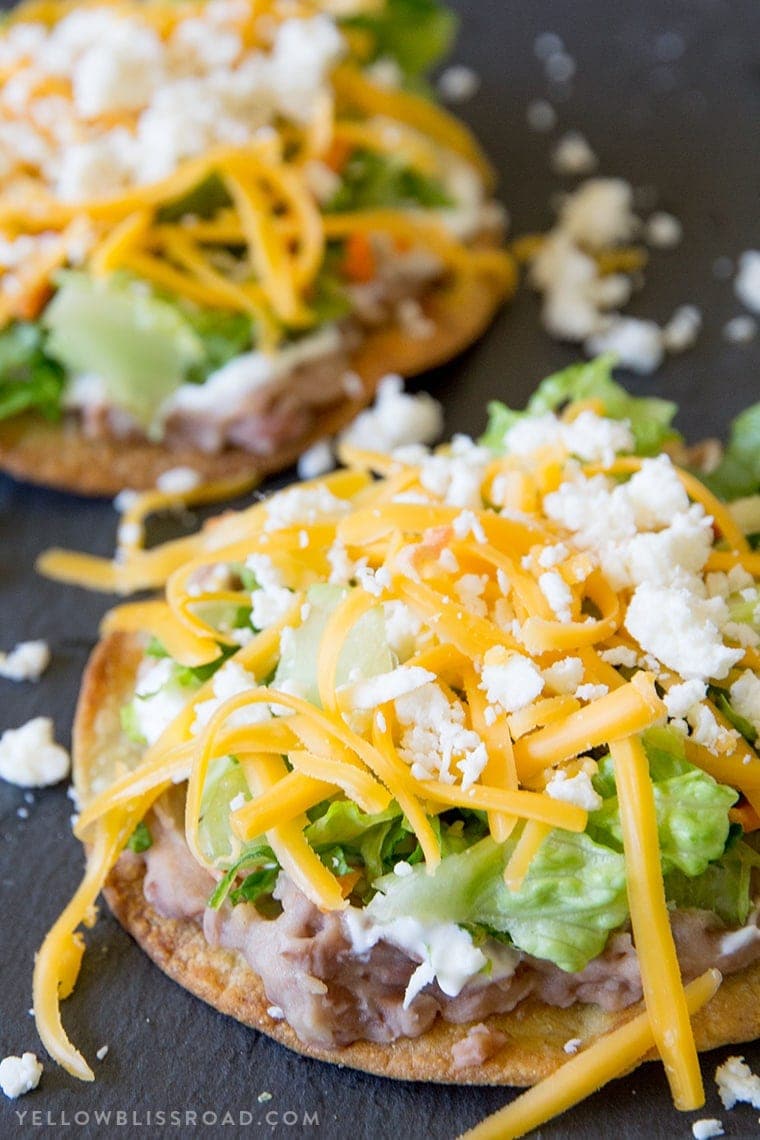 a black background with tostada shells, refried beans, lettuce, cheese.