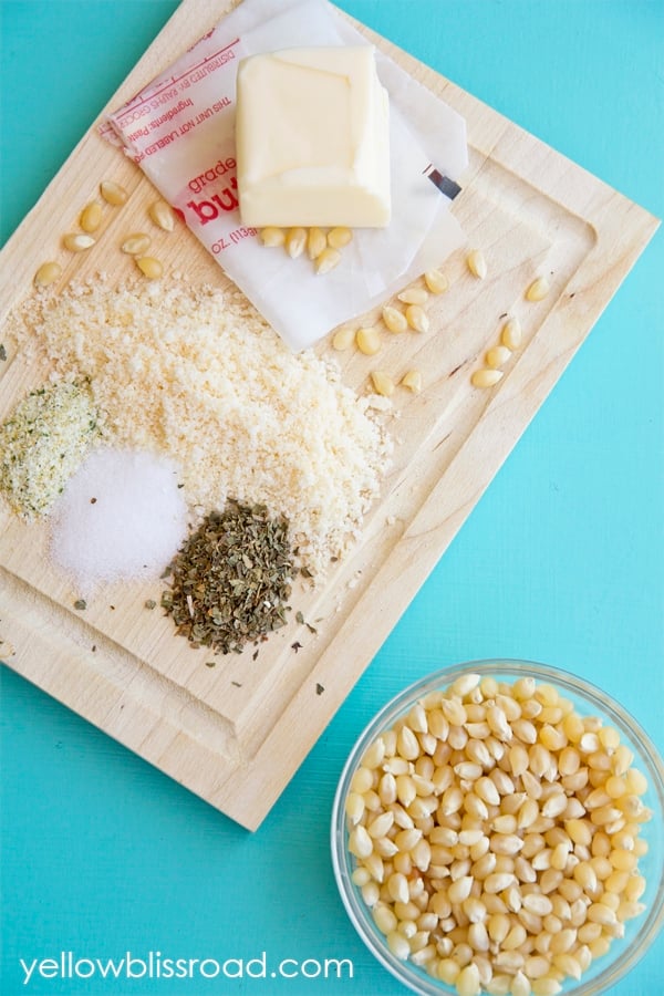 A cutting board with popcorn kernels, cheese, butter, and seasonings