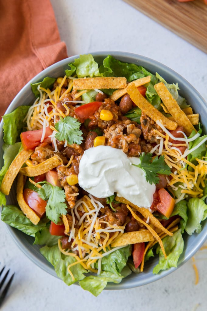 Taco salad in a bowl topped with chips, cheese, and sour cream.