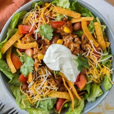 Taco salad in a bowl topped with chips, cheese, and sour cream.