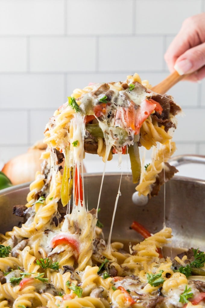 Cheesy beef and peppers pasta being scooped up by a wooden spoon