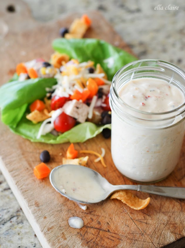 A jar of dressing next to a lettuce wrap on a wooden cutting board