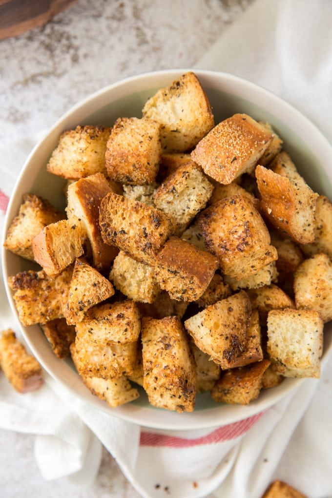 homemade croutons in a white bowl, a shite towel with a red stripe