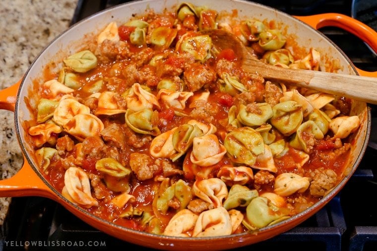 italian sausage and tortellini cooking in a large skillet with spaghetti sauce.