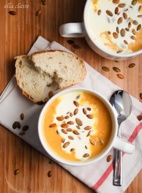 A bowl of pumpkin bisque on a wooden table, with bread