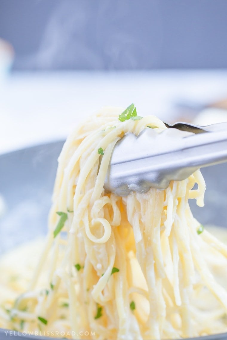 A pot of linguine with garlic parmesan sauce, tongs