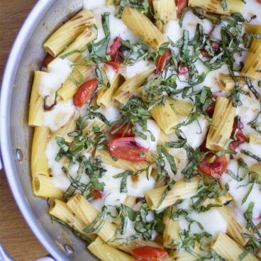 A pan of pasta with cheese, tomatoes, and basil