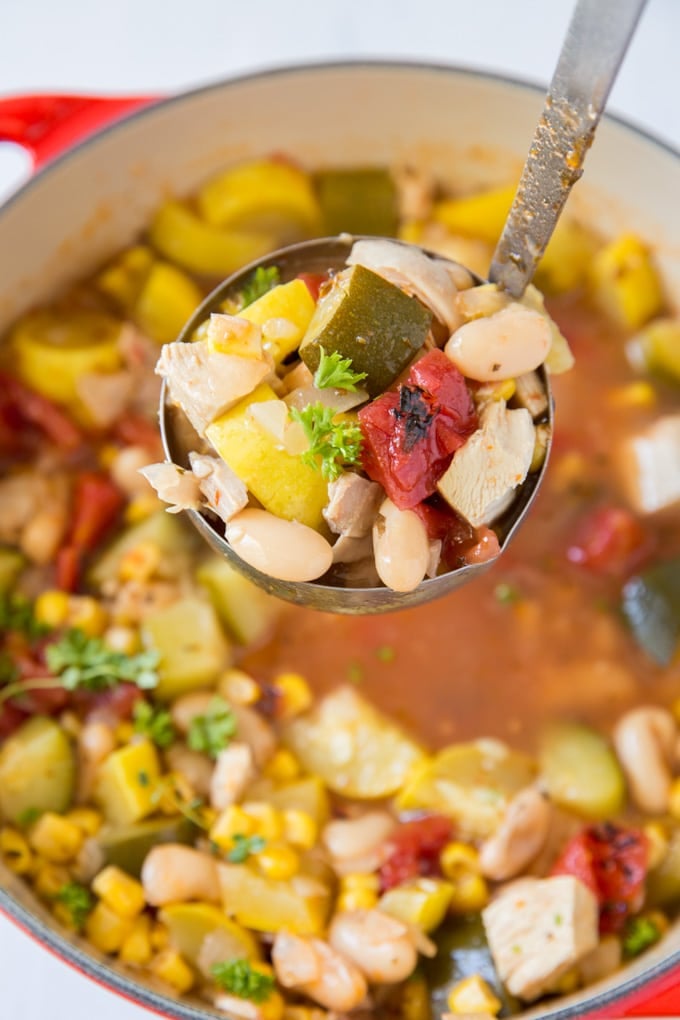 chicken, beans, tomatoes, corn and zucchini in broth held in a ladle