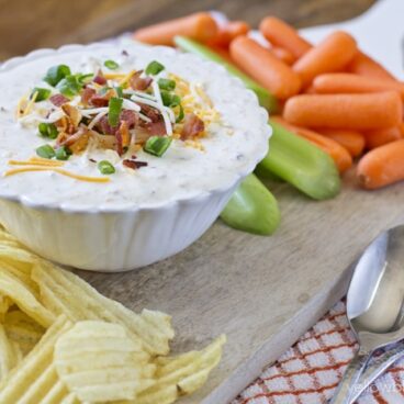 A bowl of ranch dip with carrots and chips