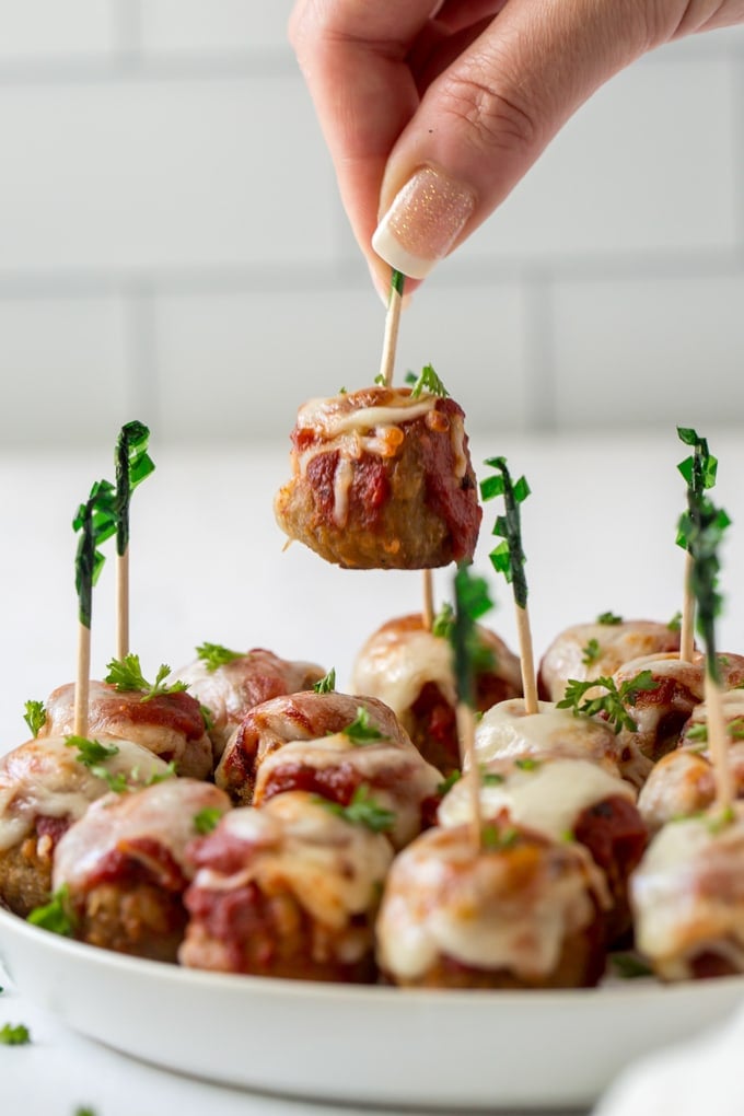 A hand reaching in and picking up a meatball appetizer off of a platter with a toothpick.
