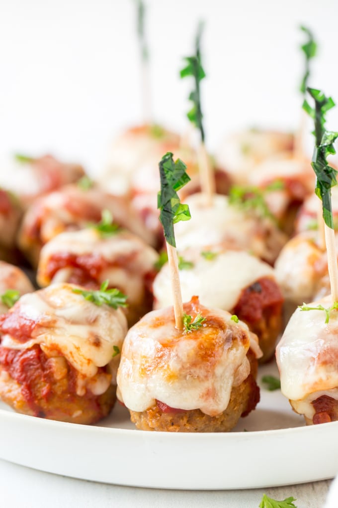 A close up image of meatballs with marinara and cheese and toothpicks stuck in them.