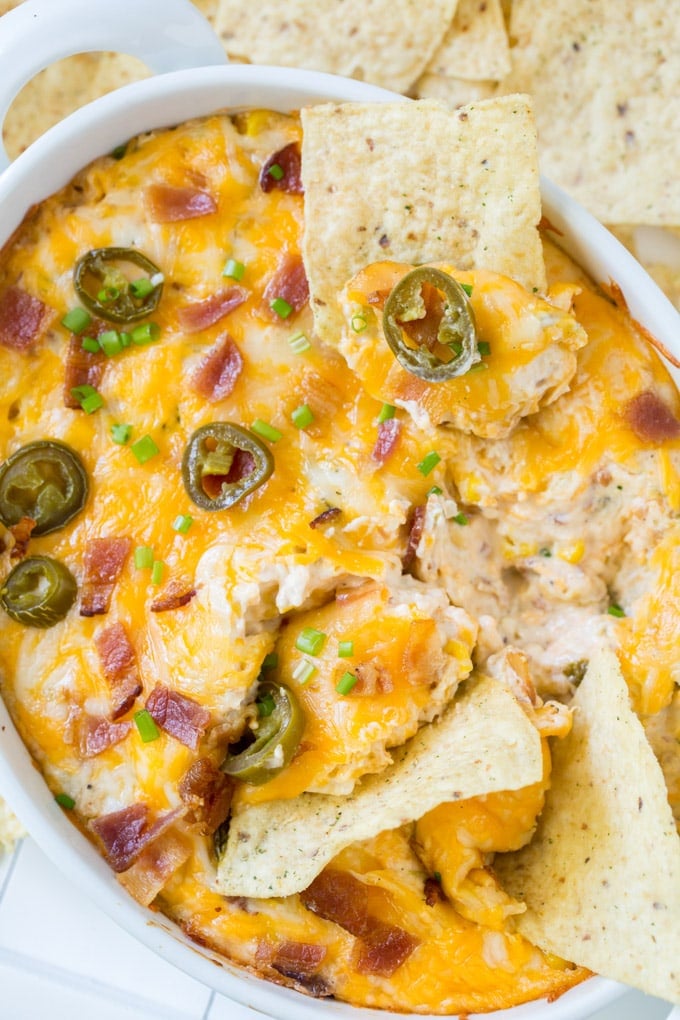 cheesy dip in a white dish with bacon and jalapenos and tortilla chips