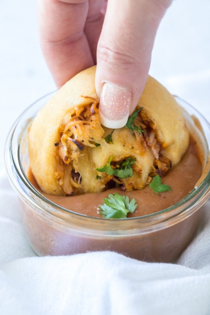 a hand holding a rolled dough pinwheel with chicken and cheese and dipping it into barbecue sauce.