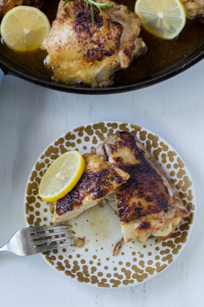 An overhead image of a chicken thigh cut in half with a slide of lemon.