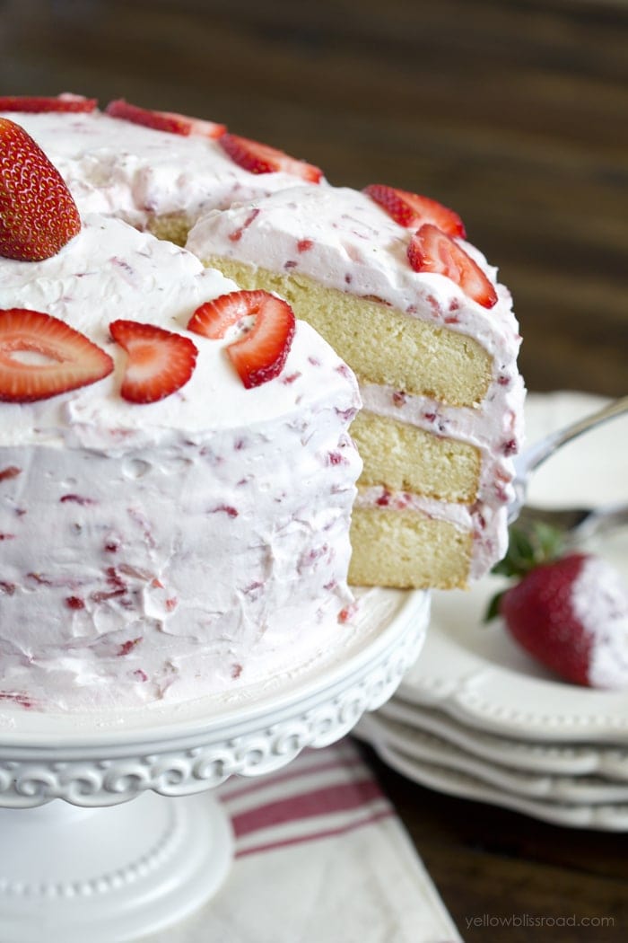 Slice of Fresh Strawberry Cake being pulled from a whole 3 layer cake