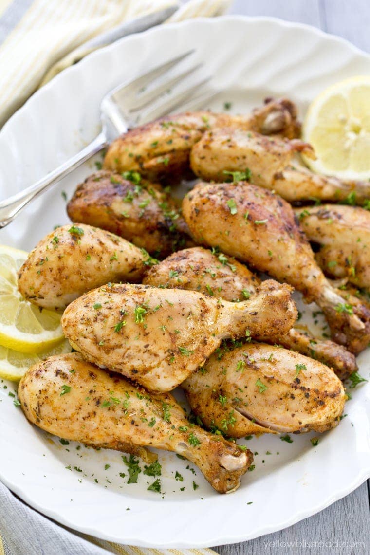 lemon chicken drumsticks baked, white platter, lemon slices, parsley, fork