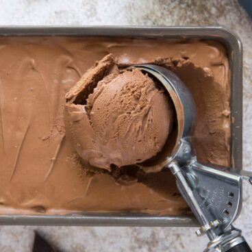 Chocolate ice cream in a pan with an ice cream scoop.