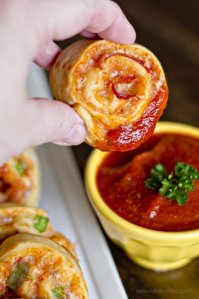 Hand holding a Pizza Pinwheel dipped in Marinara. 