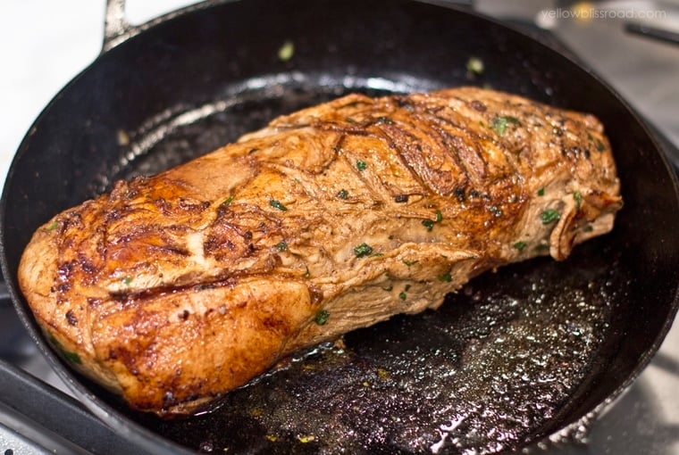 a pork loin being seared in a cast iron skillet