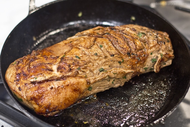 a pork loin being seared in a cast iron skillet