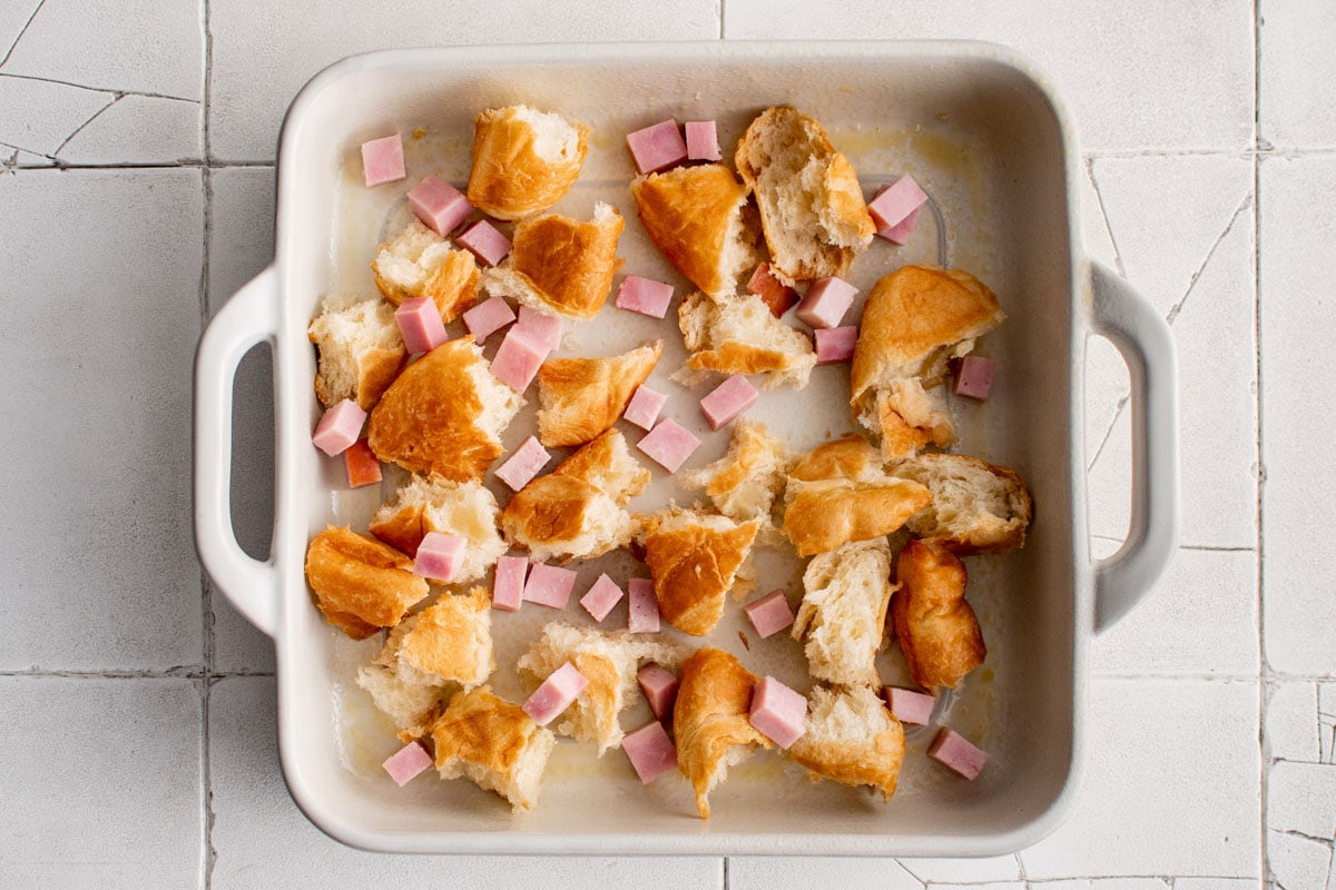 Croissant pieces and cubed ham in a casserole dish.