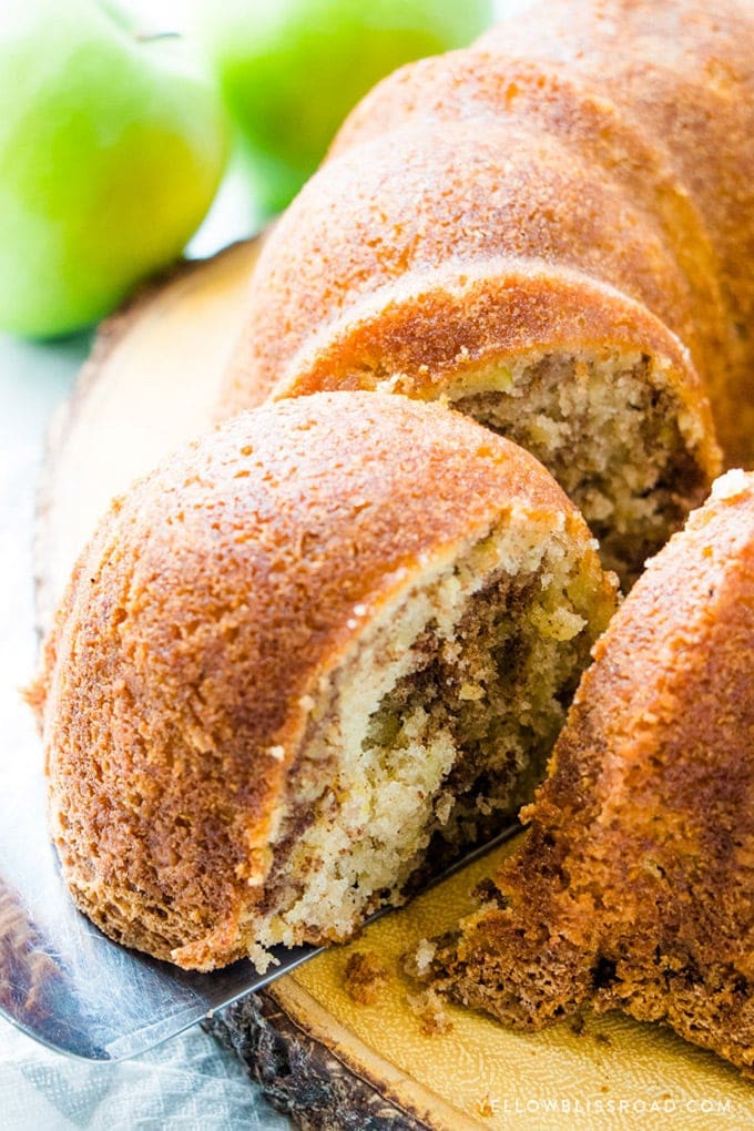 Cinnamon Apple Bundt Cake on a wood slice platter with green apples in the background.