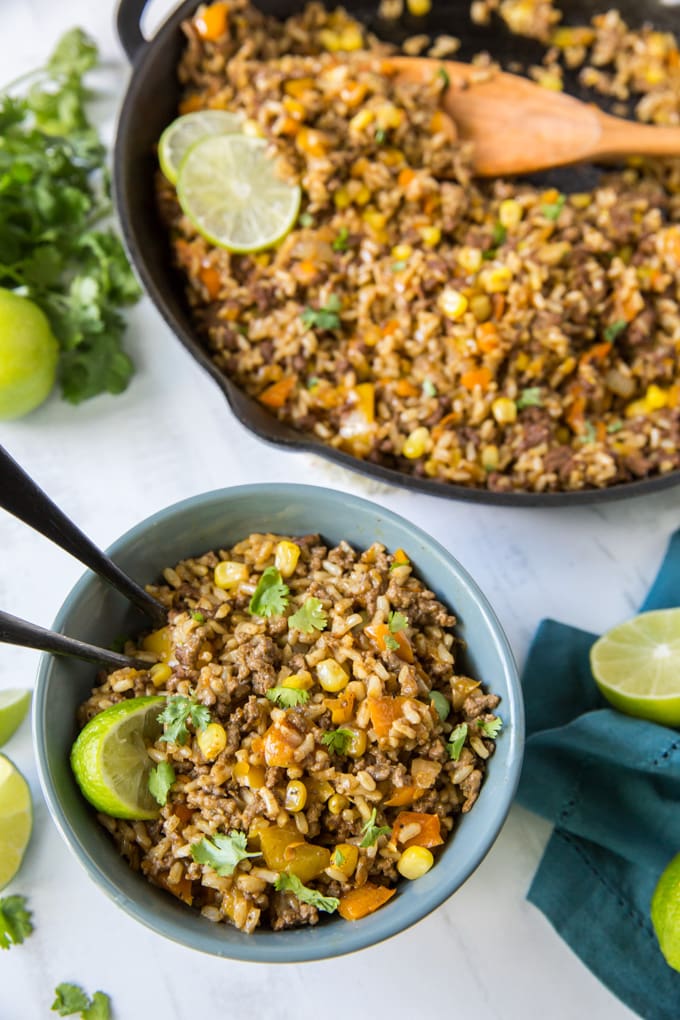 a bowl of rice with ground beef and vegetables and a skillet with the meal