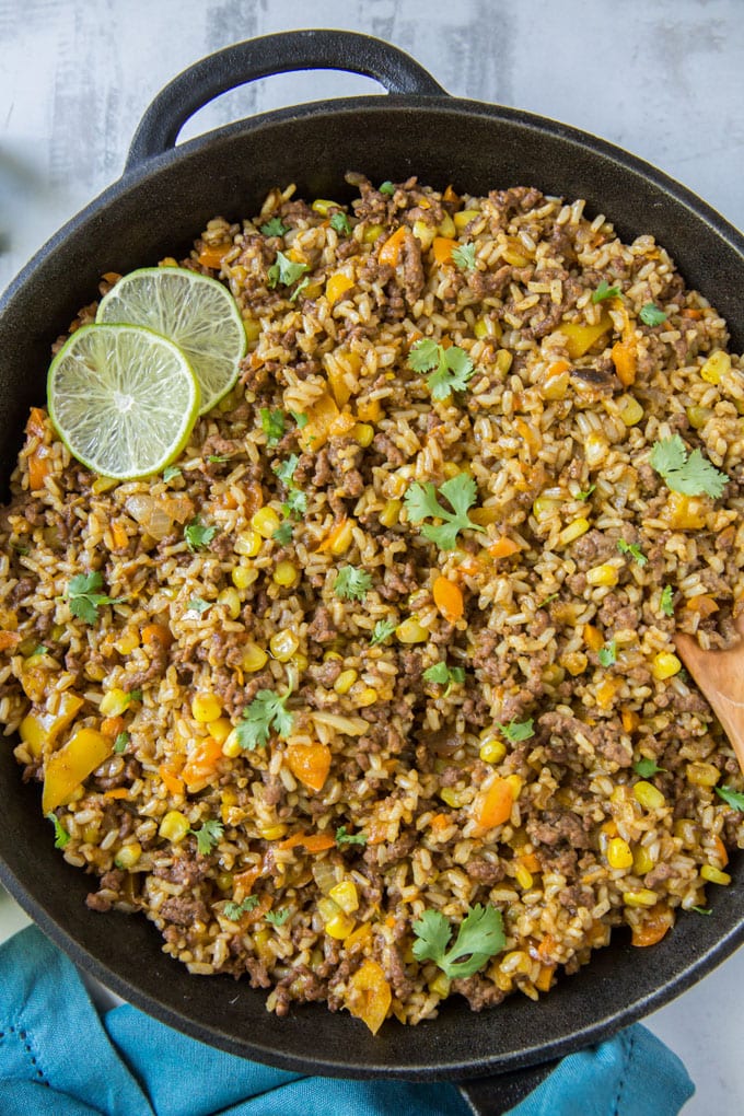 a large skillet with tex mex ground beef and rice and some sliced limes