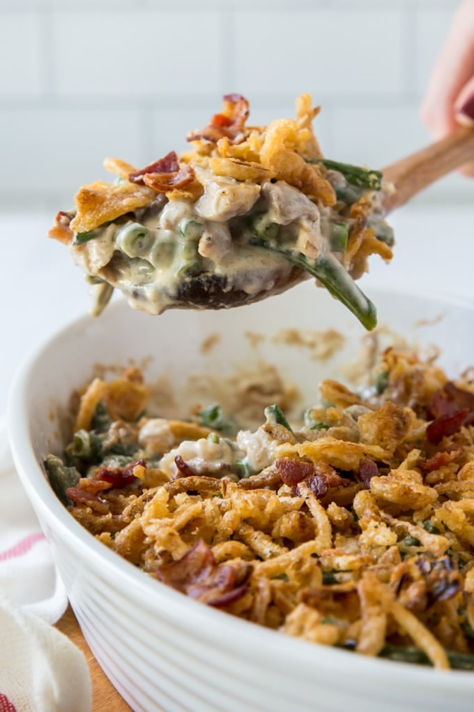 a scoop of green bean casserole on a wooden spoon help above the casserole dish