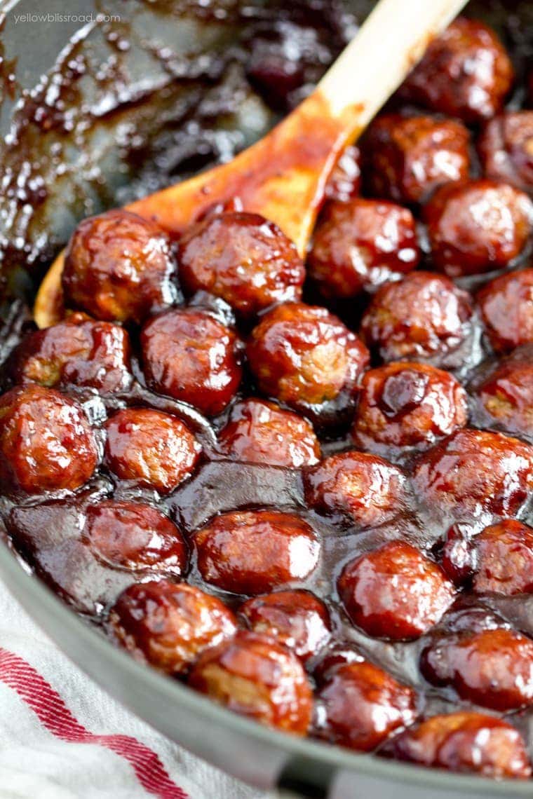 meatballs in a skillet in cranberry bbq sauce, wooden spoon