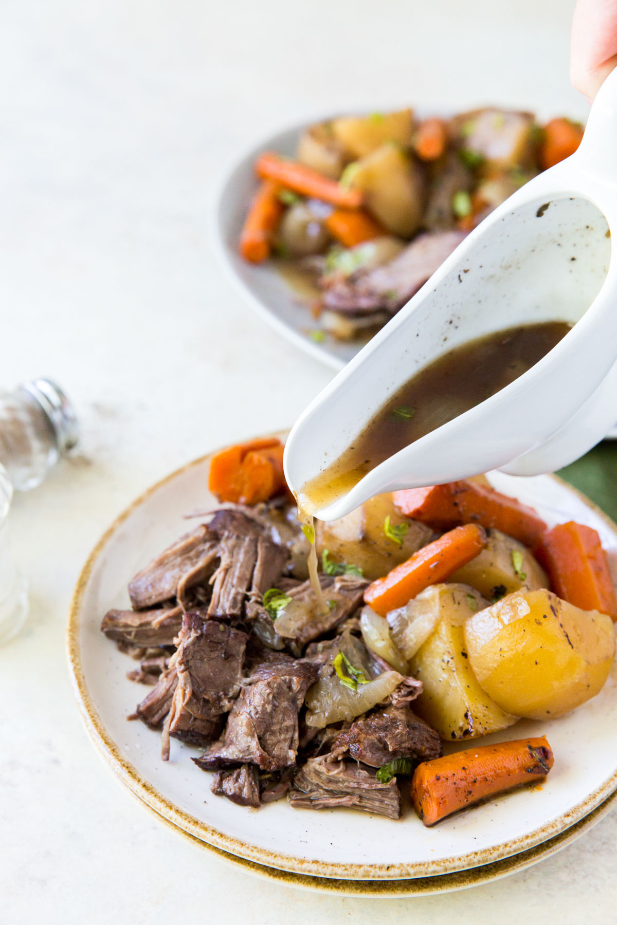 gravy in white gravy boat, white plate, pot roast, carrots, potatoes, onions