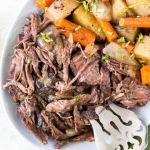 pot roast with carrots, potatoes, onions on a white plate, silver fork
