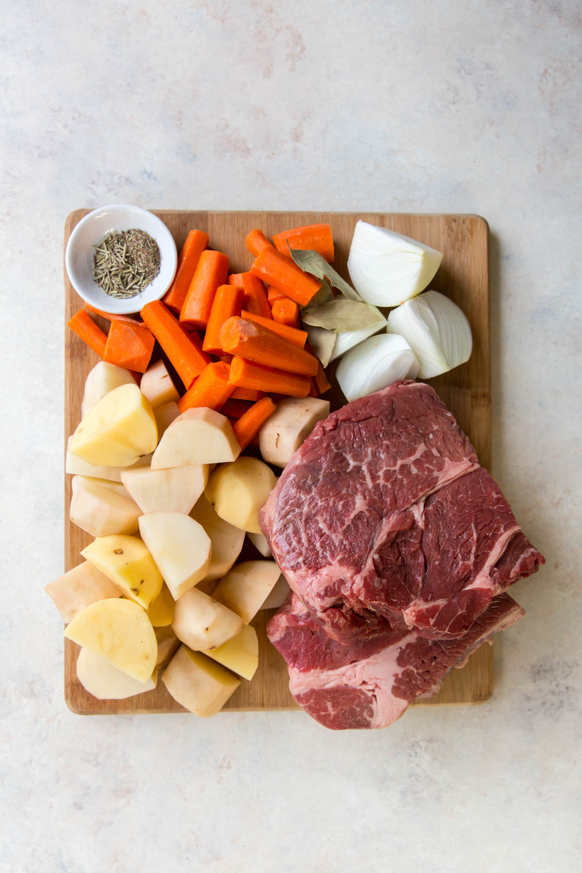 cutting board, chuck roast, potatoes, carrots, onions, herbs, spices white dish