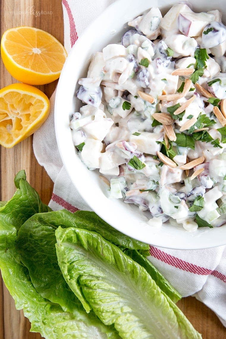 a white bowl with chicken, grapes, and sliced almonds in a creamy sauce, romaine lettuce leaves, sliced lemon.