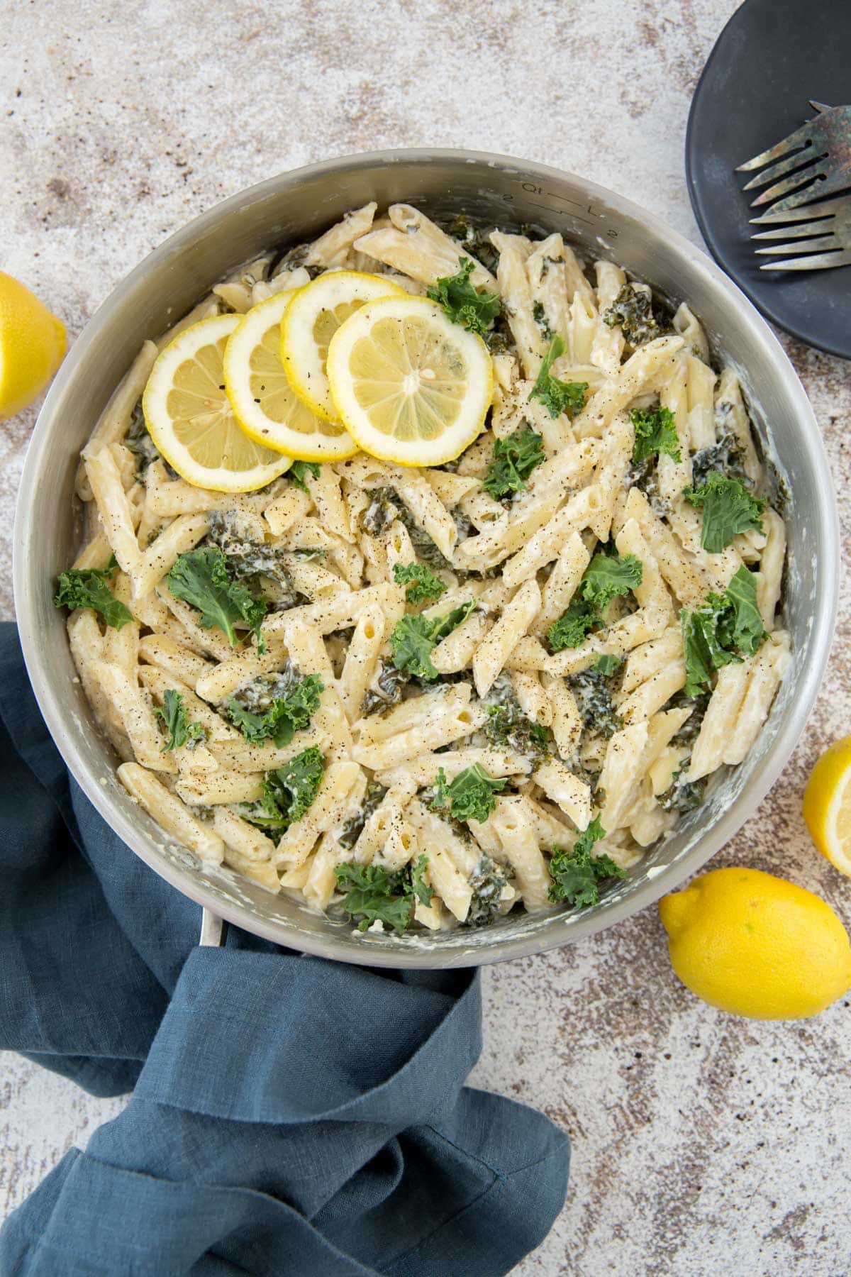 large silver saute pan, pasta, kale, lemon, blue napkin