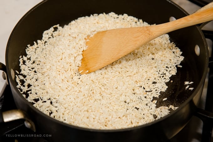 Long grain white rice toasting in a pan, a wooden spoon for mexican rice