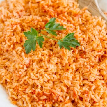 White platter filled with Mexican Rice with a wooden spoon and parsley.