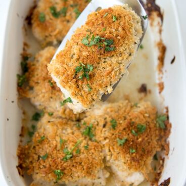 chicken breast pieces with crispy topping in a white dish. One piece held up with a spatula.